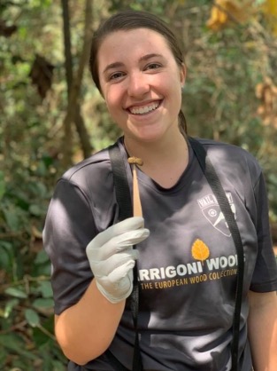 Tabor Whitney, a white woman, in the field holding a primate fecal sample on a stick. 